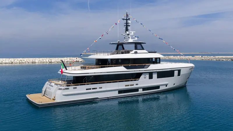 The stern quarter, with the transom platform folded down at the waterline and the flag flying at delivery.
