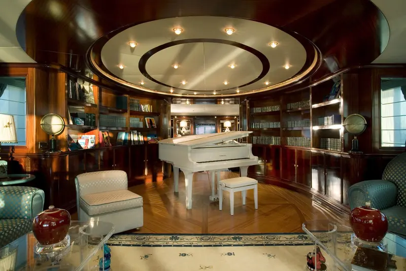 An interior library fitted out as a piano lounge, with a baby grand piano, dark wood panelling and a domed ceiling light.