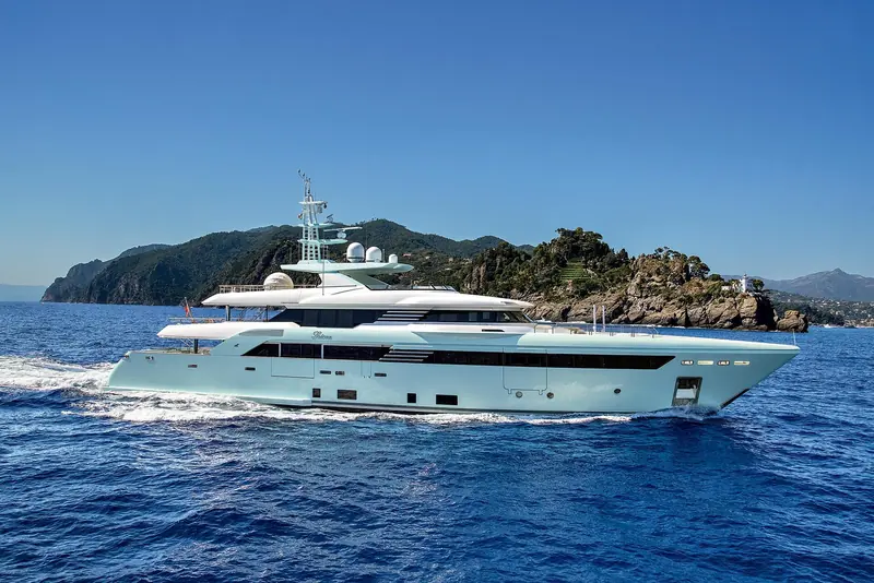 Latona underway off Portofino, the headland's characteristic rock face and pine cover behind her.