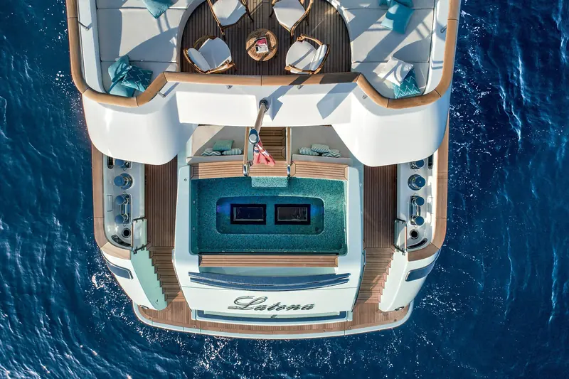 A crew member on the aft swim step beside the painted Latona nameplate, the platform extended down to the waterline.