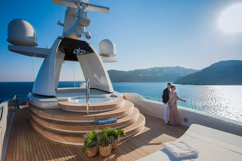 A couple descend the aft swim-platform steps together, the open sea and a distant headland behind them.