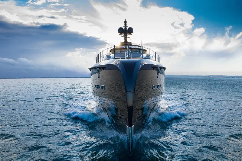 Voice cutting through the sea bow-on, spray breaking high off the flared bow in a dramatic sea-trial style shot.
