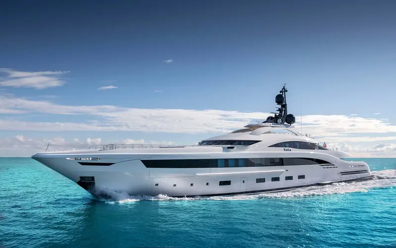 A couple stand on the aft swim platform, mountainous coastline rising behind the yacht.