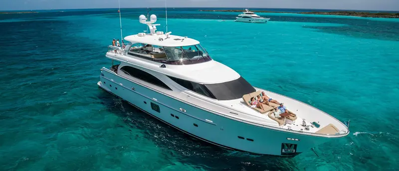 At anchor over Bahamian sand flats, the low-profile flybridge and long foredeck sunpad that define Horizon's E98 raised-pilothouse layout.