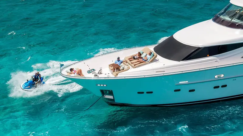 Bow-on at anchor with a jet ski alongside, showing the flared bow and the foredeck seating built into the pilothouse structure.