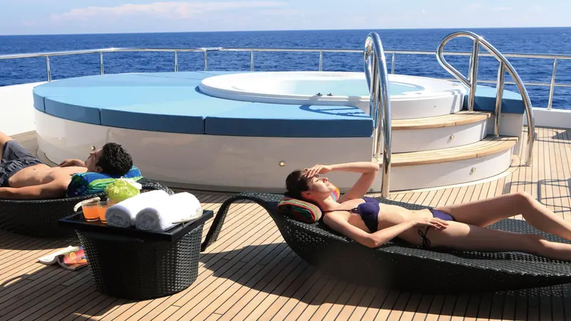 Guests using the sundeck spa pool loungers, showing the practical deck fittings: a drinks table, fresh towels and a shaded rail.