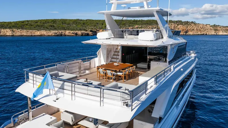 The upper deck dining table anchored off a Balearic coastline, seated for ten under the open sky deck above.