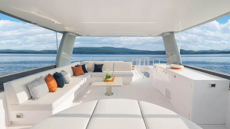 A shaded aft lounge under the flybridge overhang, upholstered in cream with contrast throw cushions.