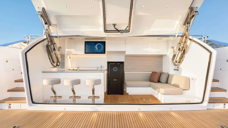 The pilothouse helm and adjoining seating, with the wheel and full electronics suite forward of the door to the deck.
