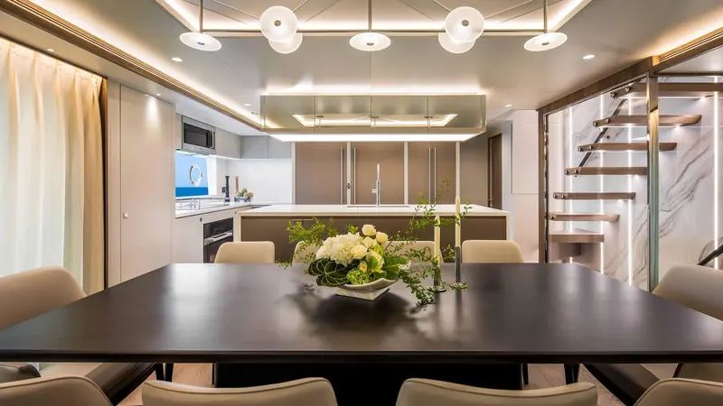 The formal dining table seated for six, positioned between the galley and a spiral stair to the lower deck.