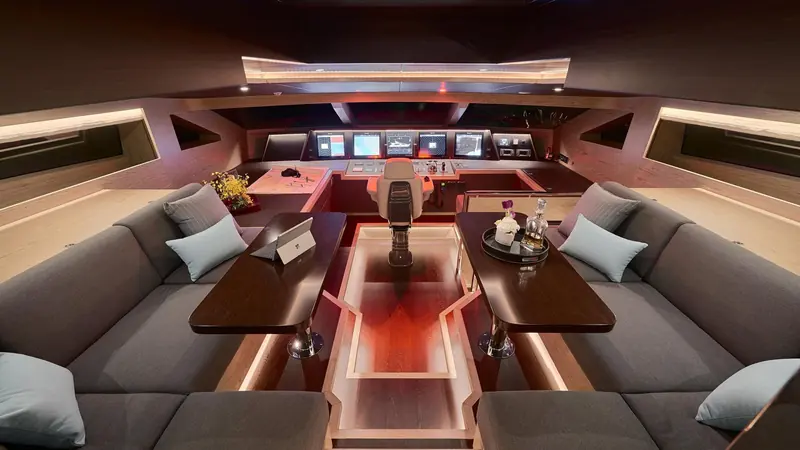 The pilothouse at night, with the full electronics suite forward and an informal seating area aft of the helm.