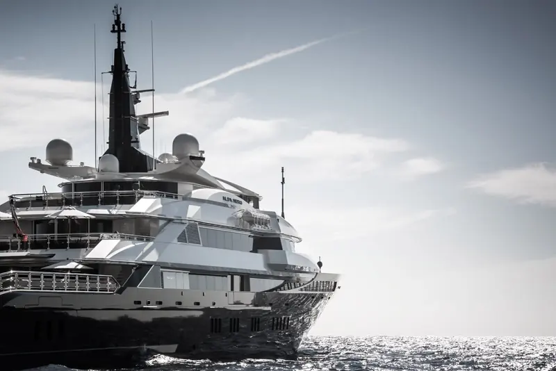 The bow close alongside, ALFA NERO lettered on the superstructure, a jet contrail crossing the sky behind her.