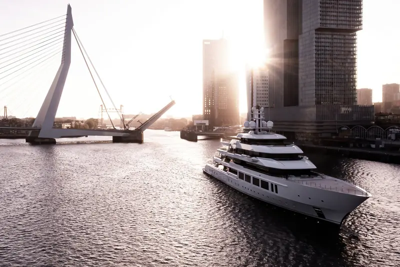 Threading the raised Erasmusbrug at sunrise, the Rotterdam skyline behind her.