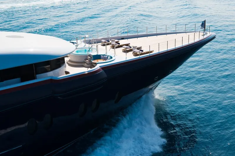 Bow-on aerial showing the forward jacuzzi and sunpad deck, spray breaking either side of the hull.