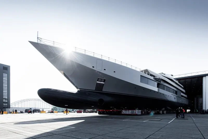 Rolled out of Oceanco's build hall on self-propelled transporters, her bulbous underwater bow extension exposed in dry dock light.