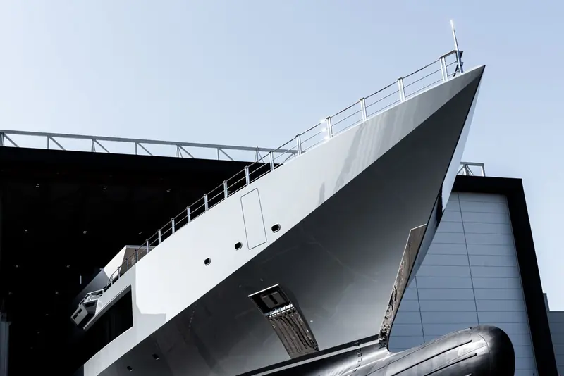 A low angle on the bow half-emerged from the shed, showing the yacht's sharply raked, faceted stem.