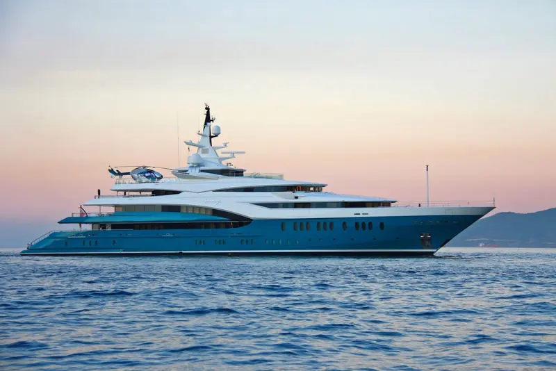 Running at dusk with the helicopter parked on the foredeck pad, sky turning orange astern.
