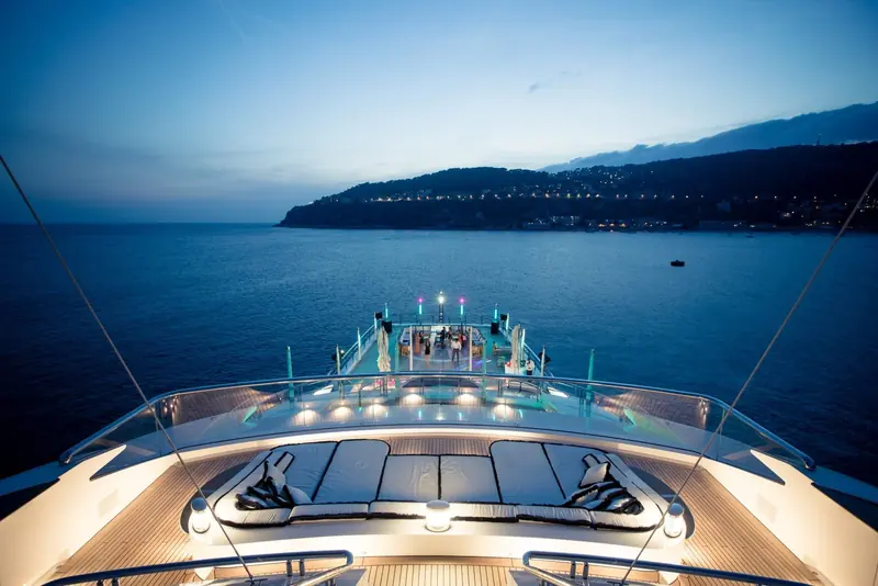 The foredeck at dusk, lounge beds and a sunken bar facing a headland anchorage on the French Riviera.