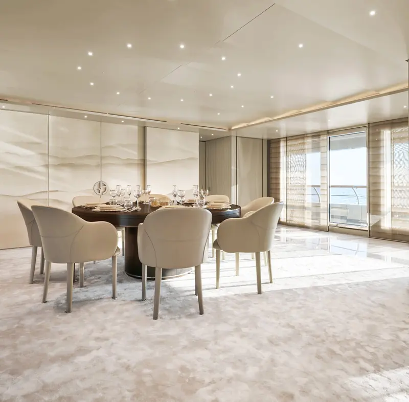 The formal dining room seats eight around a dark wood table beneath a duo-tone sand-toned wall panel, the Armani rose-gold emblem set into the bulkhead behind it.