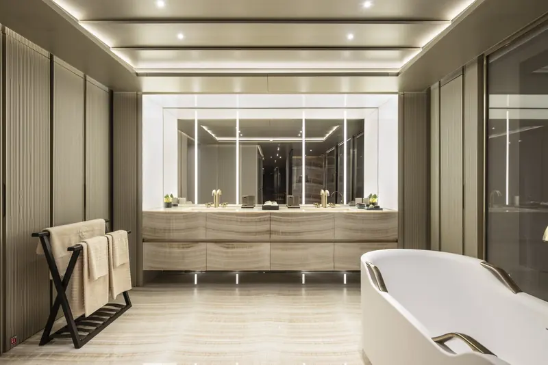 A master bathroom in book-matched onyx, twin vanities either side of a mirrored dressing area and a freestanding tub finished with the same bronze hardware as the doors.