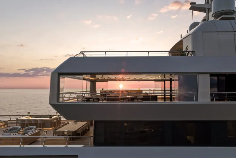Sunset through the glazed corner of the main deck lounge, the cantilevered structure over the sundeck bar giving the silhouette its distinctive notched profile.