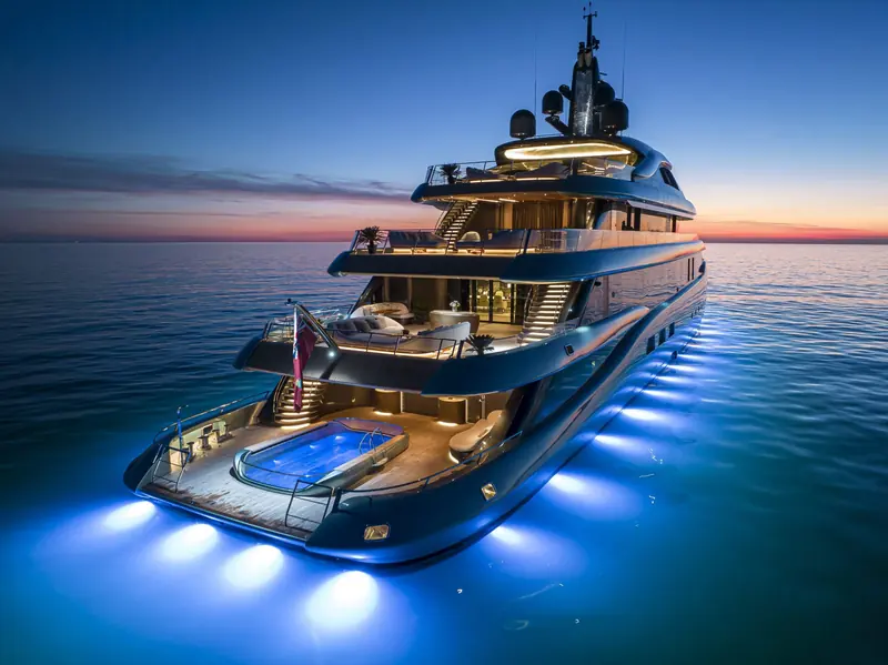 Underwater lighting turns the wake blue at dusk, with the aft beach club doors open onto the swim platform.
