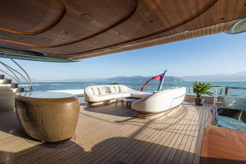A teak-lined side deck with barrel-shaped stools, framed by the coastline rather than screened off from it.