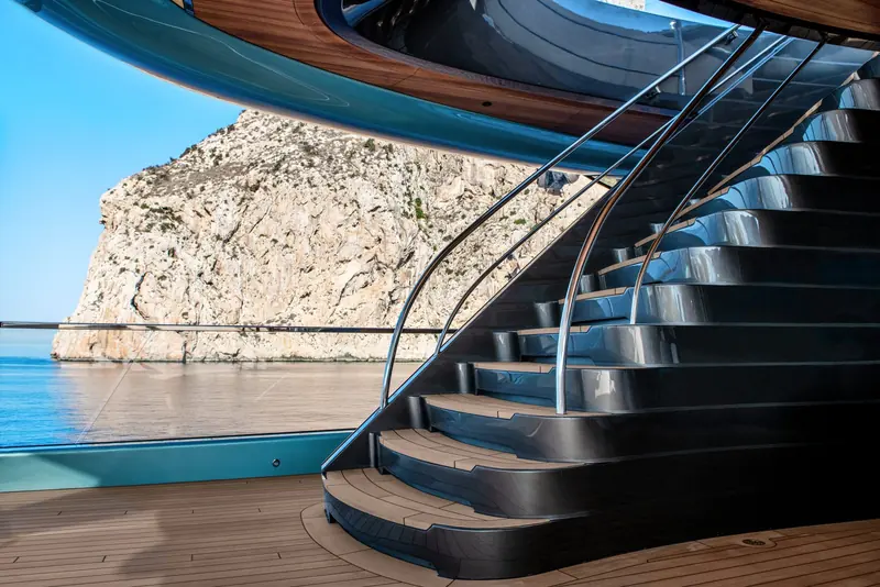 A stairwell finished in blackened metal runs alongside a plunge pool, with the cliffs of the anchorage filling the opening beside it.