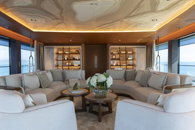 A curved lounge finished in lacquered wood panelling, its bookshelves and window line following the same radius as the hull outside.