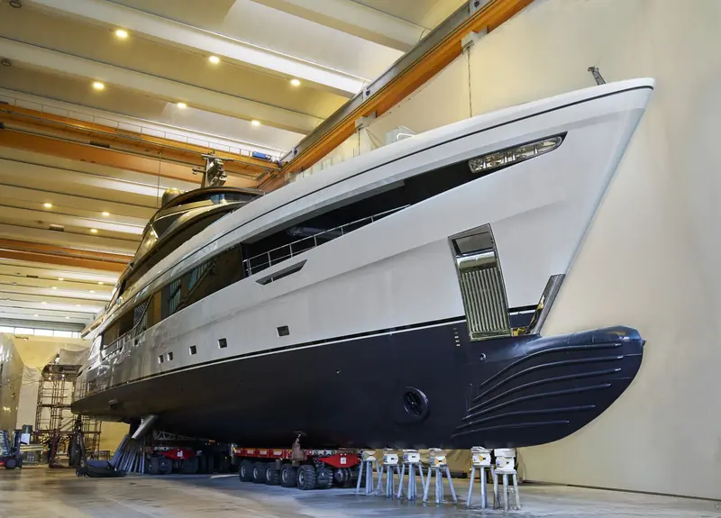 Inside the build shed ahead of transfer: the reverse bow and vertical stem of the Piredda & Partners hull design, still on cradles with the transporter's axles beneath.