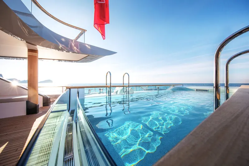 The infinity-edge pool spills toward the open sea, its steel ladder and the red signal flag catching the low morning sun.