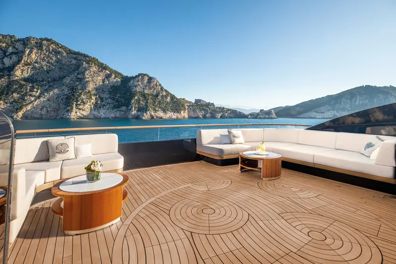 A top-deck lounge set into a teak compass-rose sole, positioned to look straight at the cliffs rather than out to open water.