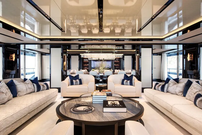 The upper saloon runs in dark lacquer and pale leather, with a full-beam mirrored ceiling that doubles the drop lighting over the seating.