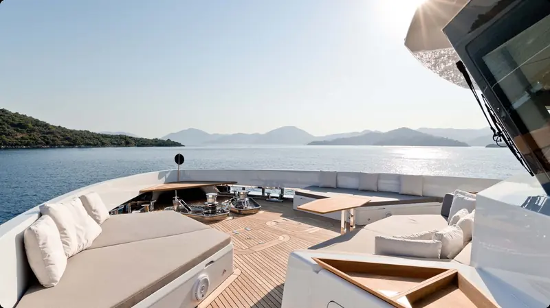The flybridge lounge looking forward, with island landscape visible through the wraparound screen and a fixed hardtop overhead.