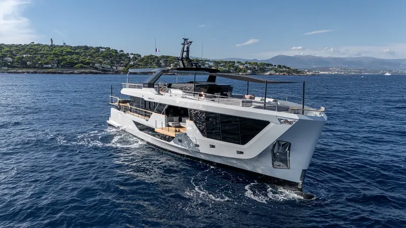 Running bow-on past the Cap d'Antibes coastline, showing the flared bow that keeps the foredeck sunpads dry underway.