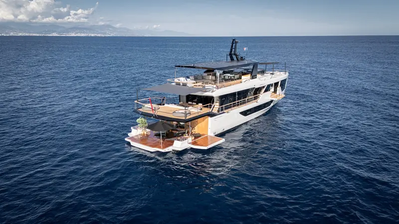 Stern quarter at anchor, side terraces folded down to widen the aft deck and the hull name Minella lettered across the transom.