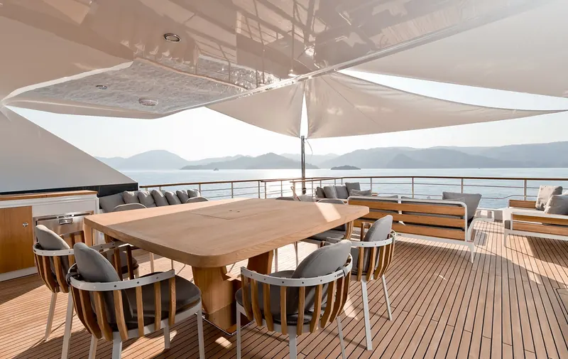 The flybridge dining table seats six under a fixed hardtop, with open rail on three sides rather than solid bulwarks.