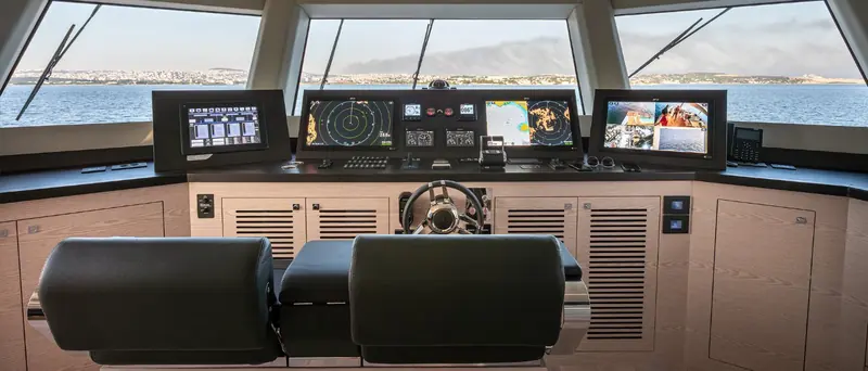 The pilothouse carries three matched displays across the console rather than one central chartplotter, with a paired helm and companion seat.