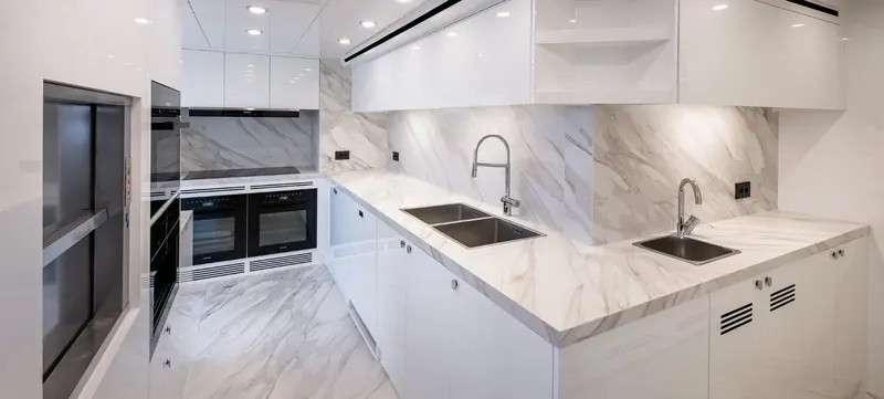 A galley finished entirely in white marble-effect surfaces, with integrated appliances rather than free-standing units.