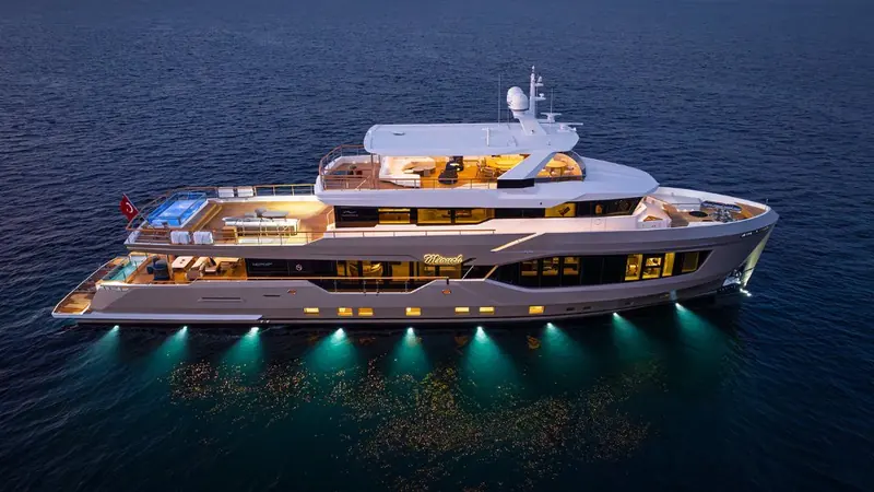 At anchor with her underwater lights on, the beach-club pool glowing green against the dark hull reflection.