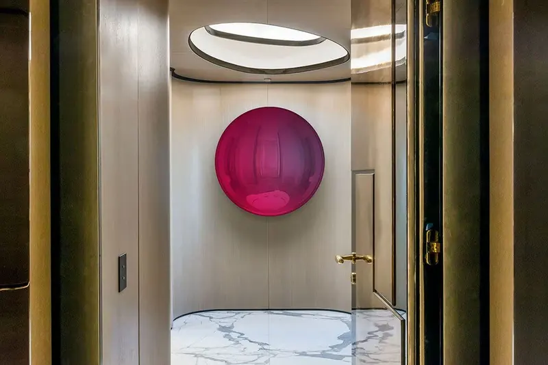 A circular skylight and a single scarlet sculpture set the tone for the lower-deck lobby in book-matched stone and bronze.