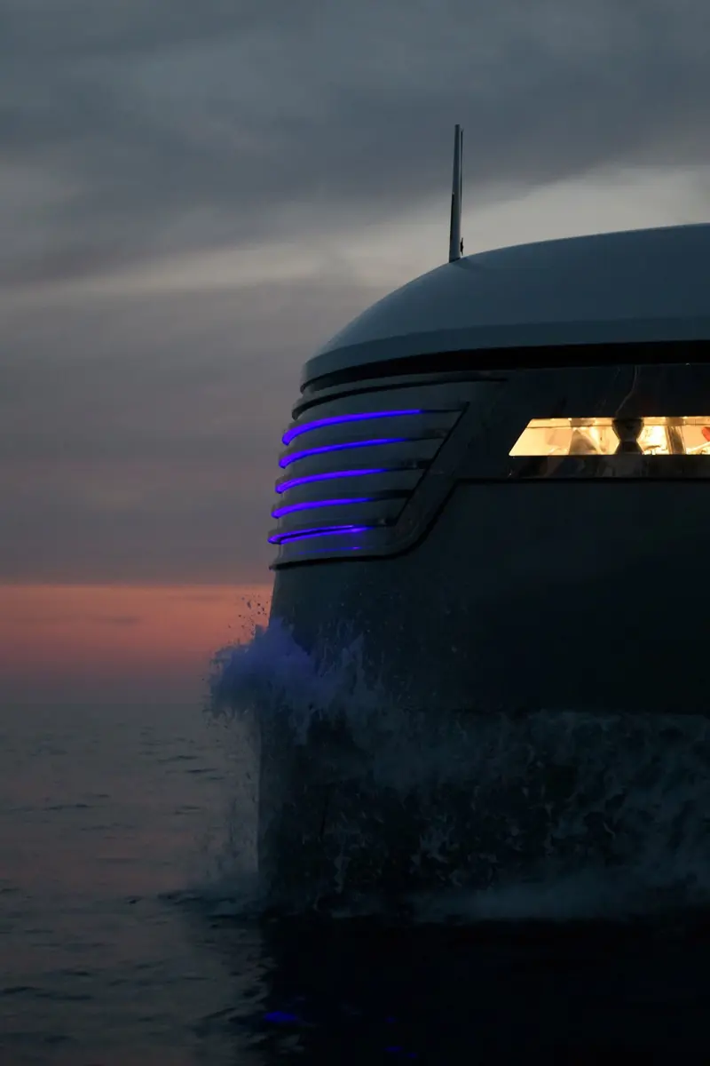 EIV's bow parting the water at dusk, indirect blue lighting tracing the raked stem as spray breaks against the hull.