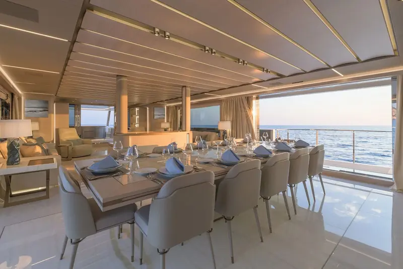 The main-deck dining table set for twelve, glass doors folded fully open to the aft deck and the sea beyond.