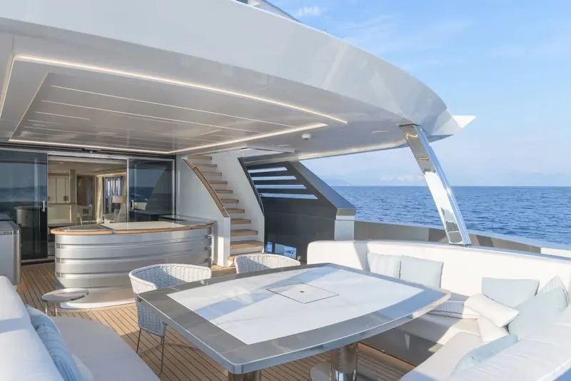 An upper-deck wet bar and dining table sit beneath the boat deck overhang, with stairs leading up to the sundeck.