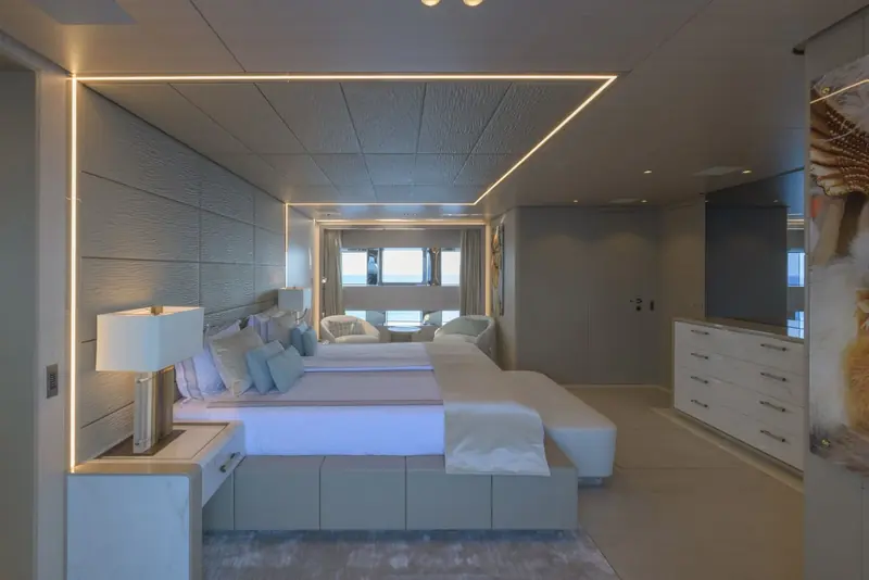A guest suite with a full-beam window seat and a stone-topped nightstand set into a backlit feature wall.