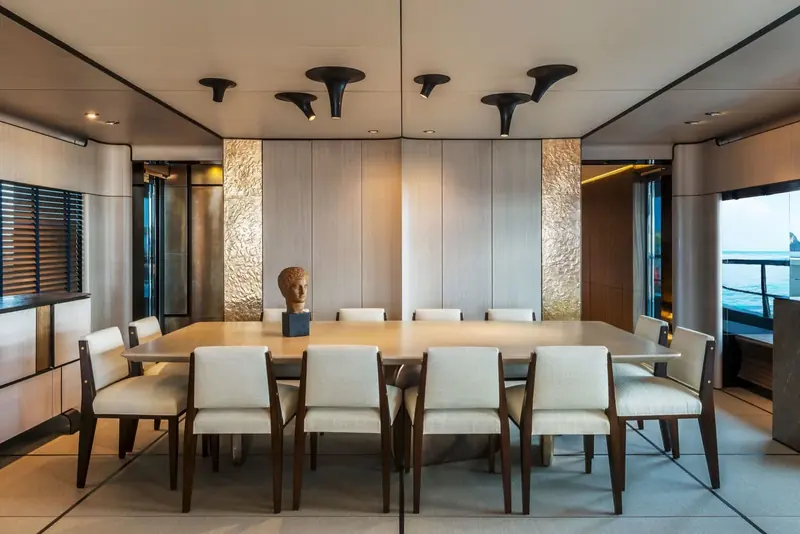 The dining room seats eight beneath a run of angular pendant lights, with a bronze figure on a plinth at the head of the table in place of a conventional sideboard display.
