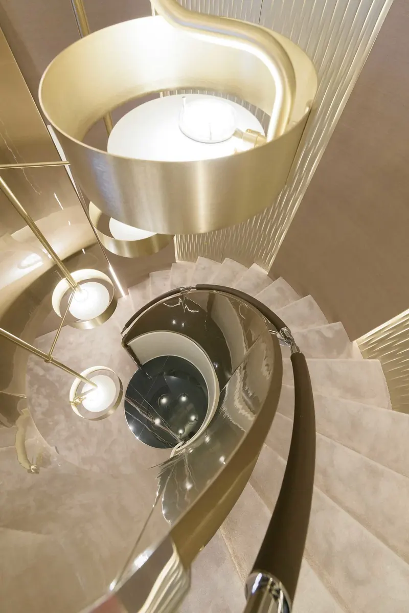 The interior spiral staircase, finished in polished steel and stone treads lit from below, connecting the decks without the boxed-in stairwell more common on yachts this size.