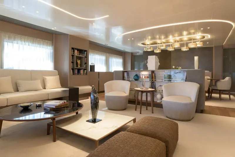 The main salon, split into a seating group forward and a bar and secondary lounge aft, both lit by a single long fixture of glass drum shades running the length of the ceiling.