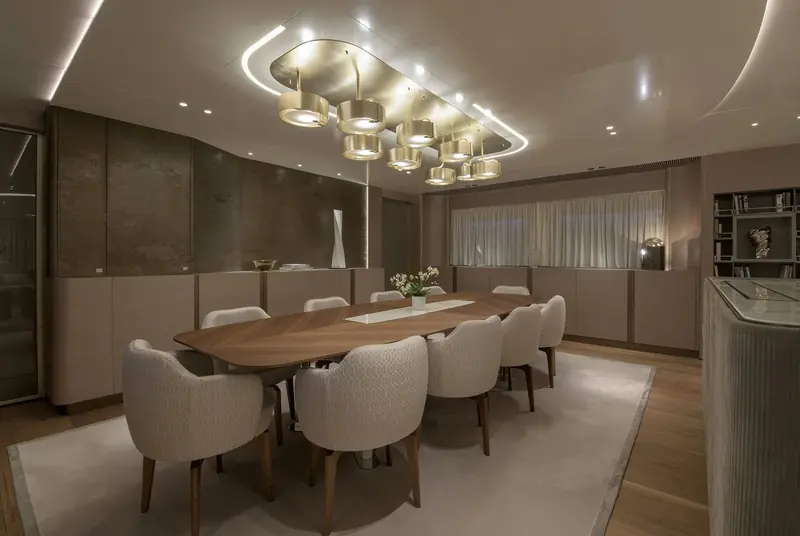 The formal dining table seats eight under a cluster of drum-shade pendant lights matching those in the salon, keeping the lighting language consistent across the main deck.