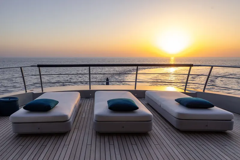 Forward sunpad facing dead into a Mediterranean sunset, the yacht's own wake catching the light astern.